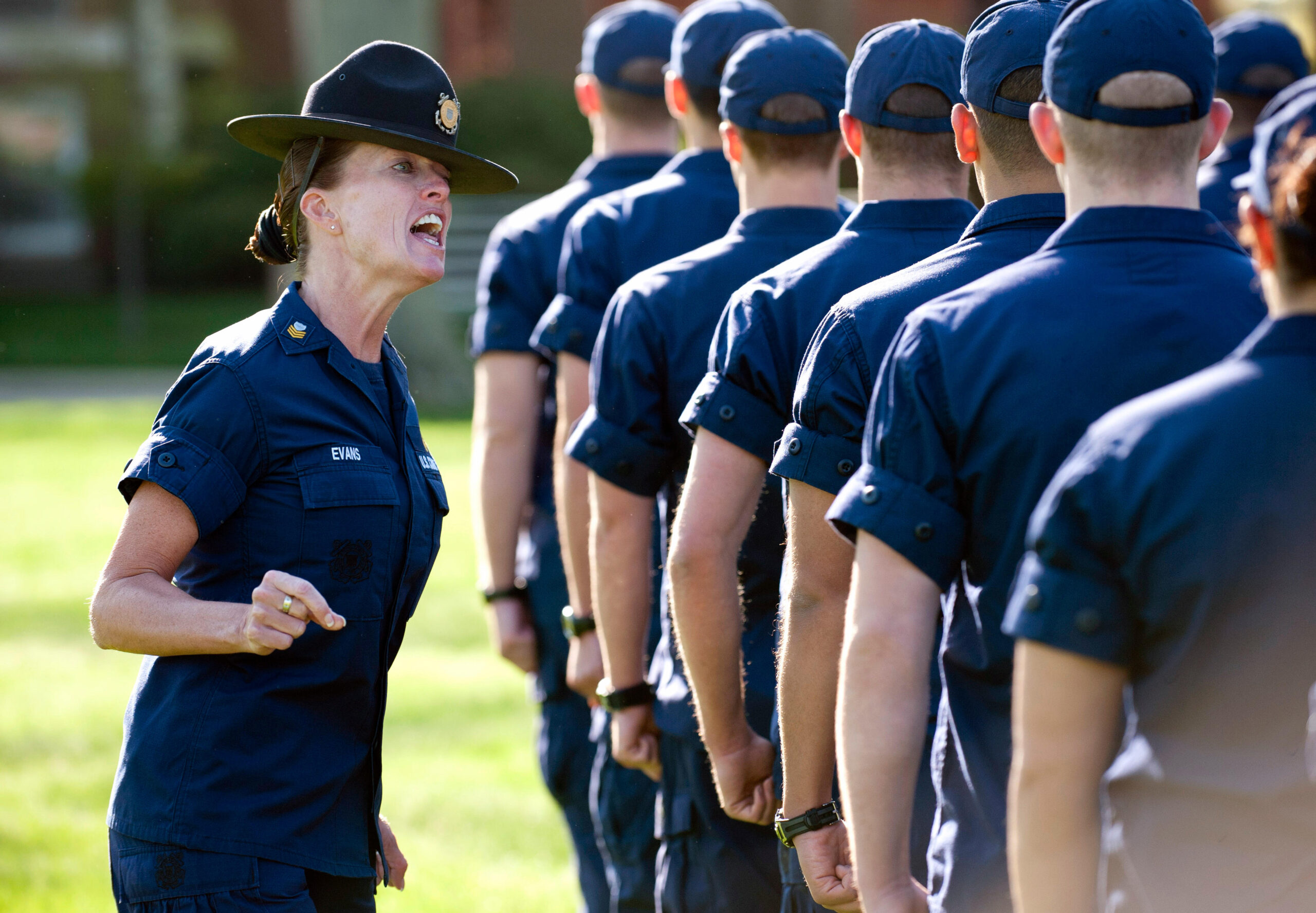 Photo: Drill sergeant motivates a group of cadets. Photo from rear of cadet grouping.